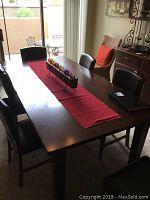 Full view of rectangular wooden dining table with six dark brown faux leather chairs and red table runner with candles