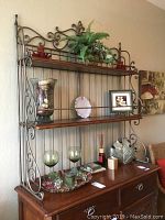 Full view of two-tier metal and wood shelf unit with various decorative items including faux plant, candle holders, ceramic plate, framed photo, and metal leaf plate on wooden cabinet below.