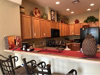 View of kitchen countertop showing red table runner, black metal candle holder, various candles, and large pineapple decorative piece approximately 12 inches tall.