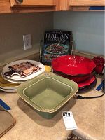 Overview of lot items showing bowls, platters, and Italian cookbook on kitchen counter.