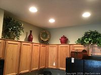 Overhead view of ceramic jars, vases, a plate, and a woven box on top of wood kitchen cabinets with plants
