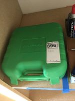 Closed green Kawasaki branded hard plastic carrying case with handle, labeled as Drill.