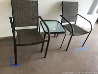 Two metal mesh chairs and one matching metal and plastic table grouped together on floor