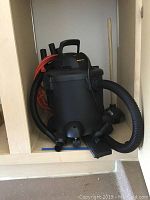 Shop Vac wet/dry vacuum showing front with the hose attached and orange power cord wrapped around it.
