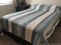 Full size bed made with striped quilted bedding in soft blue, white, and gray colors.