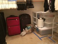View of closet corner with multiple storage items: white three-drawer plastic storage unit, several plastic storage boxes stacked on and near it, white 11-inch plastic trash can with lid on top, and soft/hard luggage pieces in red and dark colors.