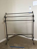 Front view of black metal quilt rack against a wall on carpeted floor.