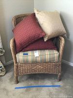 Wicker armchair with striped cushion seat and two pillows (red and beige) displayed on the chair.