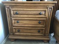 Front view of single night stand showing three drawers with decorative wood paneling and metal round knobs.
