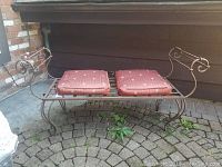 Cast iron day bed with two red patterned seat cushions, placed outside on a brick patio.
