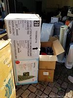 Box of 9ft Pre-Lit Sparkling Cashmere Christmas Tree with product details visible including brand, height, warm white LED lights count, and assembly instructions.