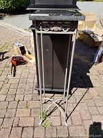 Full view of tall iron table with marble top on outdoor pavement. Shows item's size and proportions.