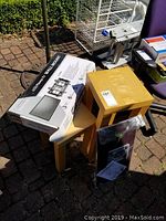 Photo showing three light wood tables stacked and boxed TV wall mount bracket on top with some other items in background.
