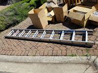 Full view of the 20ft aluminum extension ladder lying on pavement next to cardboard boxes.