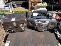 Califone vintage record player in wooden case next to Sony PDW portable CD cassette player, both on dark wooden surface outdoors.