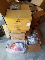 Large cardboard box labeled Nature Cup containing multiple black plastic lids individually wrapped in plastic bags, stacked inside.