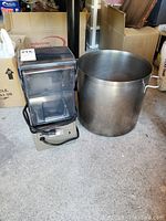 Commercial blender on left with transparent cover and power cord; stainless steel pot on right
