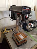 Side view of Delta 8-inch basic drill press showing rusty base, column, motor housing, and grinding stone chuck attachment.