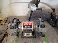 Image of front view of Ryobi 6" bench grinder showing the two grinding wheels, protective shields, on/off switch, and attached gooseneck lamp.