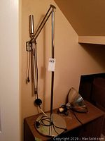 Full view of the adjustable metal floor lamp with stand and articulated arm, showing cord and base.