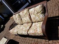 Wicker couch with patterned cushions sitting on outdoor brick surface, showing front view