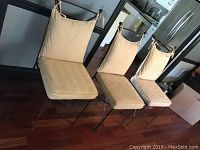 Photo showing three cast iron chairs with cream cushions set against a kitchen background.