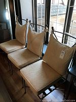 Three cast iron chairs with beige seat and back cushions placed by a window.