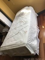 Covered twin size mattress on bed frame, white bedspread with floral embroidery seen from top down angle.