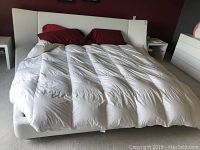 Front view of the king size white leather bed with red pillows and white comforter covering the mattress. Shows the padded headboard and low profile frame.