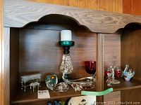 Wide view of the shelf holding all the glass items including piano, swan, whale, decorative strawberries on silver stand, red goblets and candle holder.
