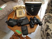 Overview photo showing various binoculars, carry case and phone on wooden table.