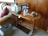 Full frontal side view of wooden sofa table set against wood panel wall next to couch. Various decorative items on table surface.