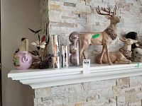 Photo showing ceramic deer figures, candle holder set, and other small decorative pieces on a white mantel with stone tile wall.