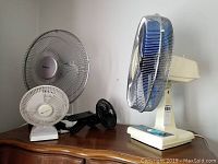 Three table top fans and one clip-on fan on a wooden surface against a white wall