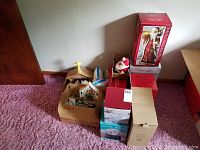Image showing several boxed and unboxed holiday decorations including a nativity scene stable, a snowman plush, and multiple red and green Christmas boxes.