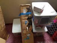 Stack of four plastic totes filled with Christmas decorations, with a cardboard box for Noma lighted decorative lamp post shown beside them.