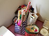 Photo showing several bags and totes containing rolls of colorful wrapping paper, boxed gift bows, and a white bag with Halloween and other holiday items inside.