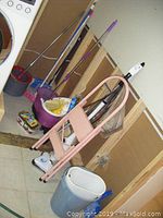 Photo of mops, broom, pink metal step ladder, and buckets on a laundry room floor.