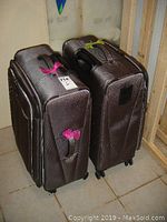 Two brown Travelpro suitcases standing upright on tiled floor, showing side and top handles.