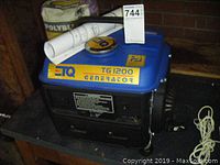 Blue ETQ TG1200 generator with yellow and black labels, including a rolled-up manual on top.