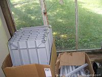 Box of stacked gray plastic shelves with grid reinforcement bottoms shown inside an open cardboard box.