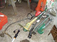 Wide view of 5 gardening tools including Homelite gas trimmer, Weed Eater electric trimmer, green leaf blower, and cordless trimmers on ground showing condition and handles