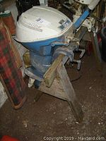 Side view of motor mounted on wooden saw horse stand showing white and blue two-stroke engine housing and mounting clamps.