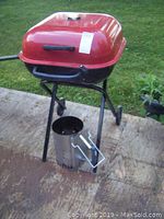 Photo of red and black Aussie charcoal grill on patio with Weber charcoal starter below the grill