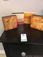 Four encaustic wax art pieces displayed on black table, showing abstract warm-toned patterns