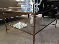 Full view of coffee table showing metal frame with decorative legs and glass top with lower glass shelf.