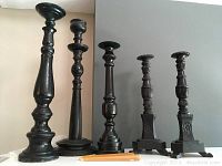 Full view of all five black wooden candlesticks arranged by height on a flat surface with candles placed at base for scale.