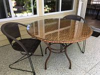 Outdoor round wicker and glass table with metal base and two matching plastic wicker and metal framed chairs.