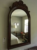 Front view of the antique wood framed mirror hanging on a wall, showing the full mirror and carved top detail.