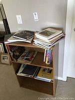 Front view of the wood laminate bookcase showing three shelves with assorted books on top and inside.
